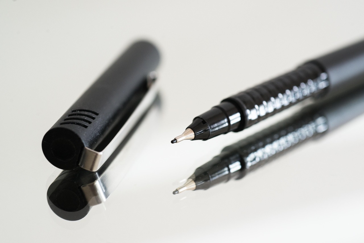 Two pens mirrored on a reflective white surface